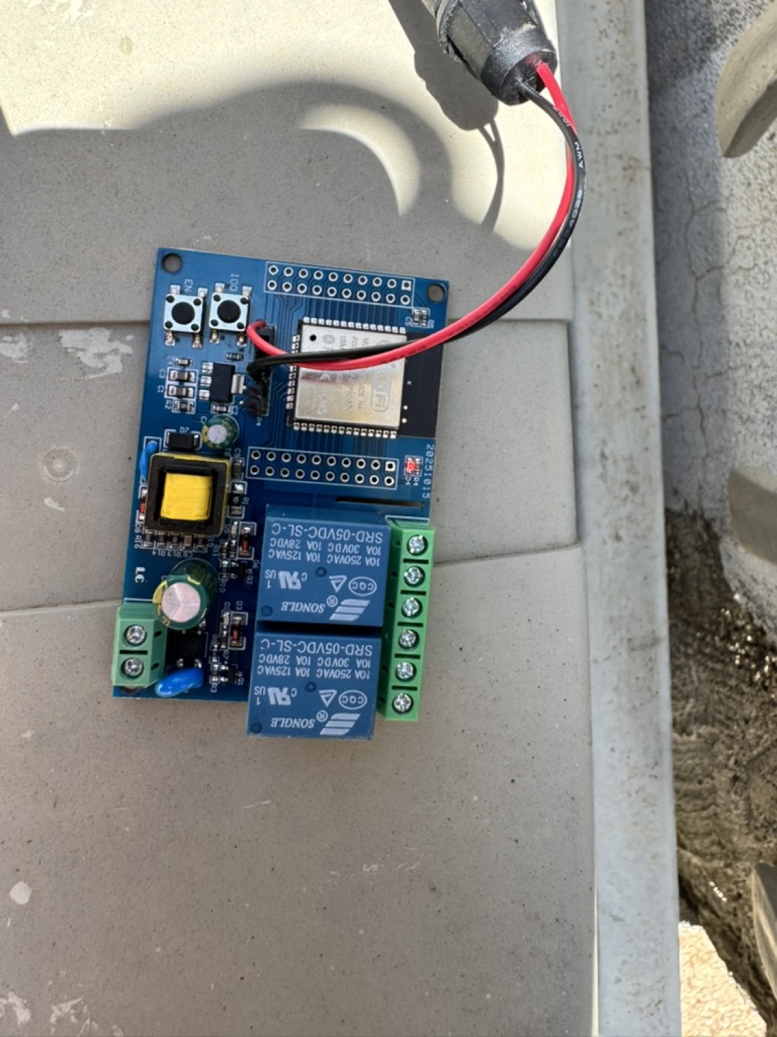 The ESP32 relay board mounted at the gate, powered by red and black wires from a supply